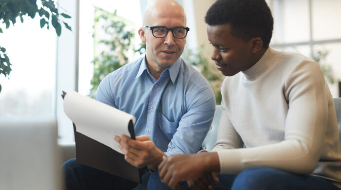 Portrait of bald mature businessman talking to young trainee while working on internship project, copy space