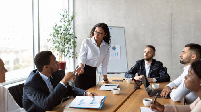 Businesswoman Giving Speech On Business Meeting With Colleagues, Discussing Work Ideas And Projects, Making Presentation Standing In Modern Office. Teamwork, Entrepreneurship, Corporate Meeting