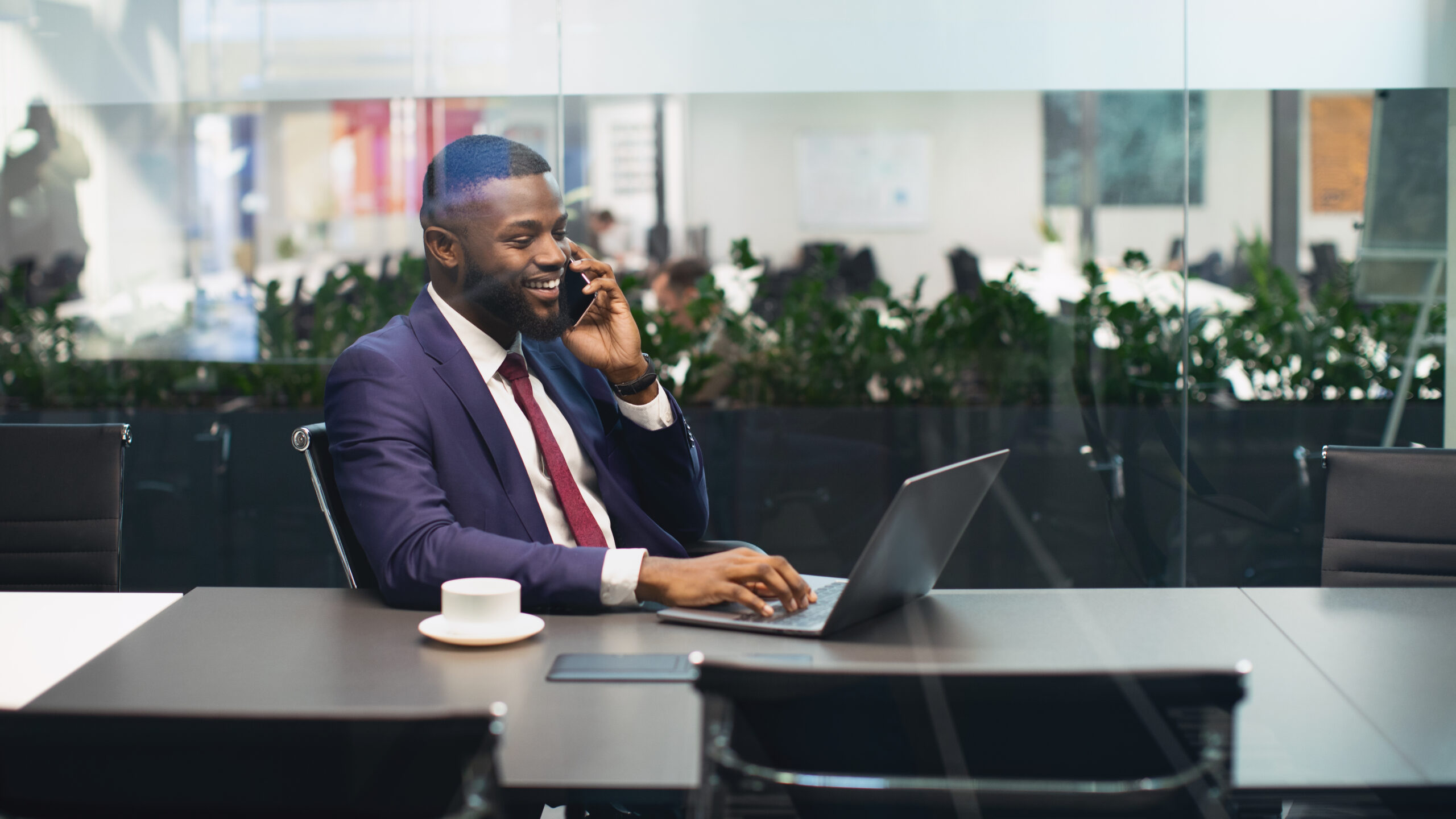 Cheerful Black Businessman Working On Laptop, Having Phone Conversation