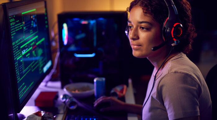 Female Teenage Hacker Sitting In Front Of Computer Screens Bypassing Cyber Security