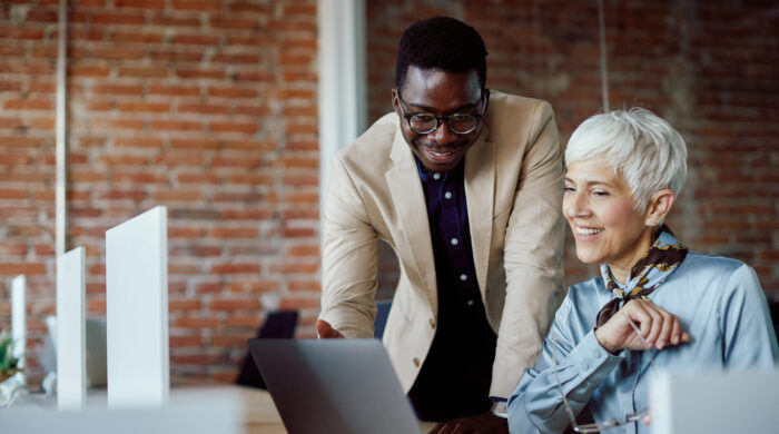 Happy African American businessman and his mature colleague using laptop while working in the office.