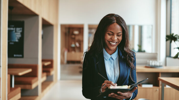 Young African American businesswoman laughing and writing notes in her day planner while walking in a bright modern office