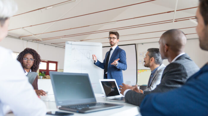 Low angle shot of speaker talking and looking at colleagues. Group of workers discussing ideas during presentation of new project at briefing. Business meeting concept